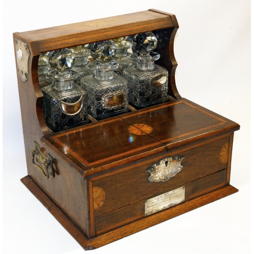 1139 - Edwardian Sheraton Revival satinwood banded oak presentation tantalus, three square decanters with s... 