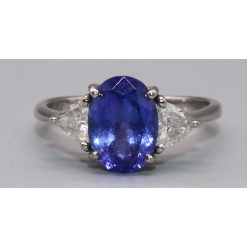 1002 - Platinum three stone tanzanite and diamond ring, the central oval cut tanzanite flanked by two trian... 