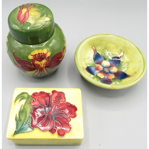 Moorcroft Pottery: 'Hibiscus' pattern rectangular trinket box and cover, red flowers on yellow ground, L9.5cm; 'Columbine' pattern footed bowl, blue and yellow flower on green ground, D11.5cm; and a small ginger jar with red and yellow flowers on green ground, H11cm (3)