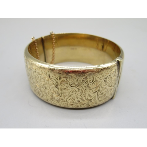 32 - 9ct yellow gold cuff hinged bangle, with half engraved foliage decoration, with safety chain, stampe... 