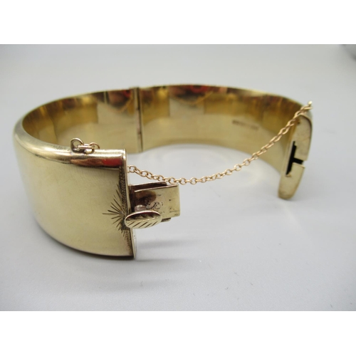 32 - 9ct yellow gold cuff hinged bangle, with half engraved foliage decoration, with safety chain, stampe... 