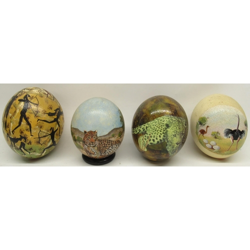 1122 - Four decorated ostrich eggs, one on turned wooden stand, 14cm.