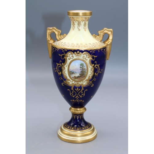 1631 - Coalport porcelain two handled urn, decorated with a lake scene vignette, within blue and gilt borde... 