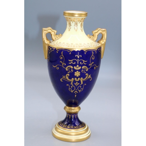 1631 - Coalport porcelain two handled urn, decorated with a lake scene vignette, within blue and gilt borde... 