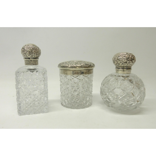 1136 - Three Victorian cut glass dressing table containers, the hallmarked Sterling silver lids with repous... 