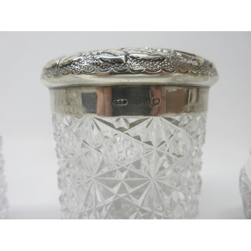 1136 - Three Victorian cut glass dressing table containers, the hallmarked Sterling silver lids with repous... 