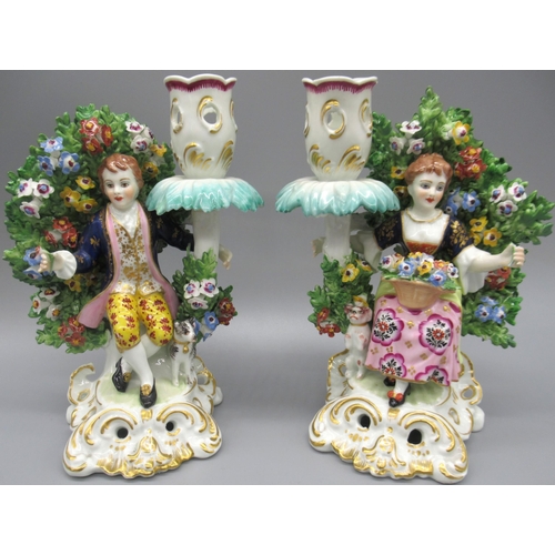 1172 - Pair of Derby style porcelain candlesticks, modelled male and female figures seated before bocage, o... 