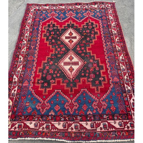 677 - 20th Century Caucasian wool rug, two central geometric medallions within red field and geometric bor... 