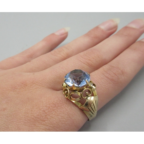 1052 - Yellow metal cocktail ring, large blue stone set in ornate mount, marks indistinct, size Q, 3.9g

Br... 