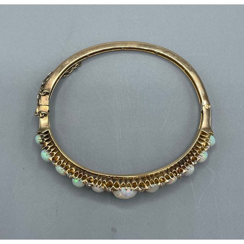1004 - 19th century 18ct yellow gold opal and diamond hinged bangle, decorated with a row of eleven graduat... 