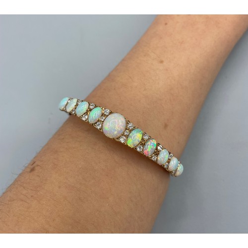 1004 - 19th century 18ct yellow gold opal and diamond hinged bangle, decorated with a row of eleven graduat... 