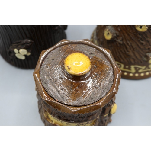 1019 - Three barkware tobacco jars of varying sizes, one in dark treacle type glaze with applied branch stu... 