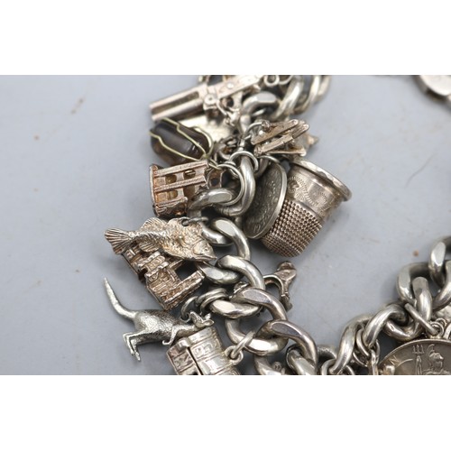 24 - Large, heavy charm bracelet comprising a thick-gauge solid curb link hallmarked sterling silver brac... 