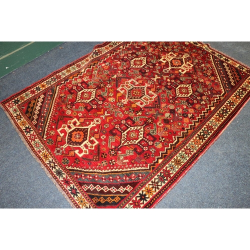 497 - Eastern red ground fringed rug with multiple gul field, 215cm x 115cm 