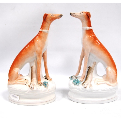 203 - Pair of Staffordshire seated greyhounds, each with a hare at their feet, 21.5cm high.