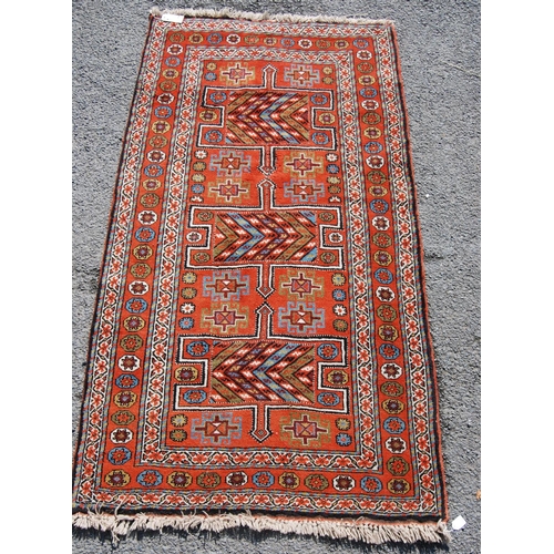 387 - Quchan rug with three H-shaped panels over red ground, rosettes and border, 112cm x 211cm.