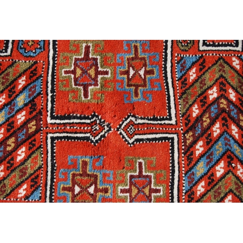 387 - Quchan rug with three H-shaped panels over red ground, rosettes and border, 112cm x 211cm.