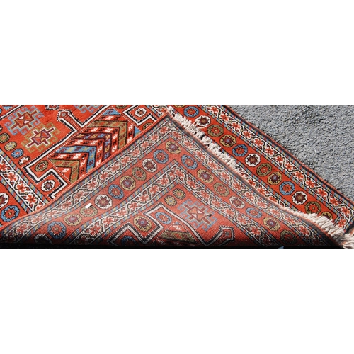 387 - Quchan rug with three H-shaped panels over red ground, rosettes and border, 112cm x 211cm.