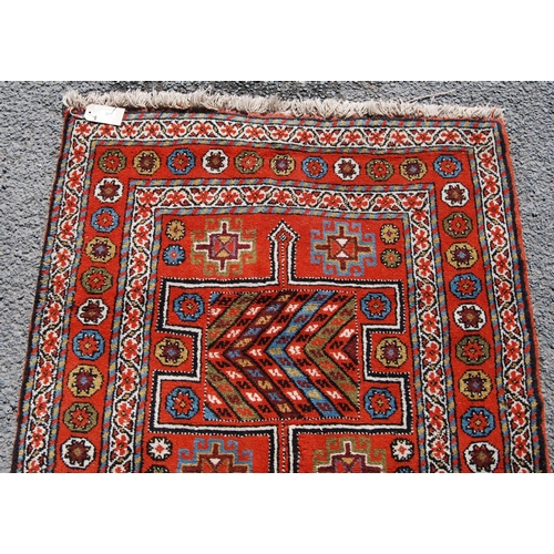 387 - Quchan rug with three H-shaped panels over red ground, rosettes and border, 112cm x 211cm.