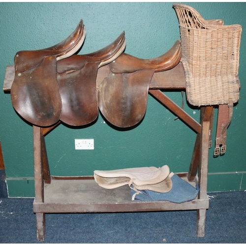 536 - Antique scumbled pine saddle stand, 145cm long, also three leather saddles and a wicker child's seat