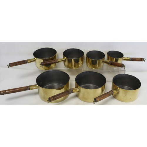 238 - Graduated set of seven brass saucepans with tinned interiors and turned wooden handles, the largest ... 