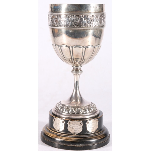 22 - Victorian sterling silver prize cup, on hardwood stand, the cup with chased border of figures, Elkin... 