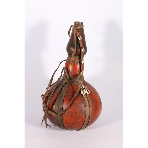 396 - African gourd water carrier with applied leather strap decorated with cowrie shells and beads, 34cm ... 