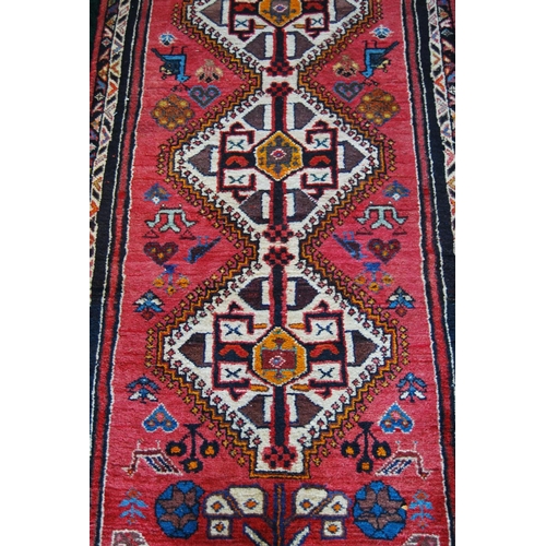 302 - Qashqai hand-knotted runner decorated with four geometric medallions on red ground, 230cm x 136cm.