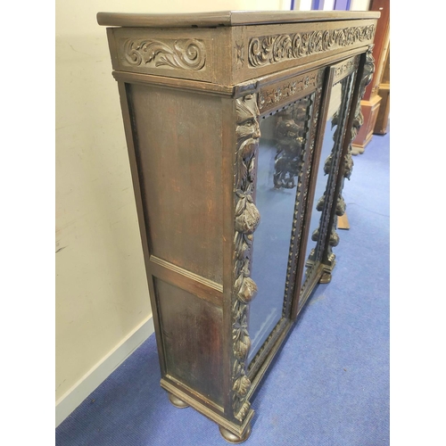 497 - Victorian stained oak glazed bookcase with twin doors, carved with mask heads , fruit, flora and fol... 