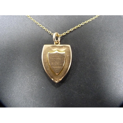 258 - 15ct gold shield-shaped locket, 13.1g, on yellow metal chain attachment.