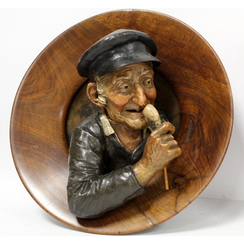 380 - Pair of Continental pottery and treen wall plaques, depicting an elderly man with a pipe and a woman... 