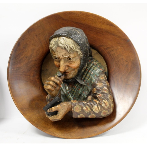 380 - Pair of Continental pottery and treen wall plaques, depicting an elderly man with a pipe and a woman... 