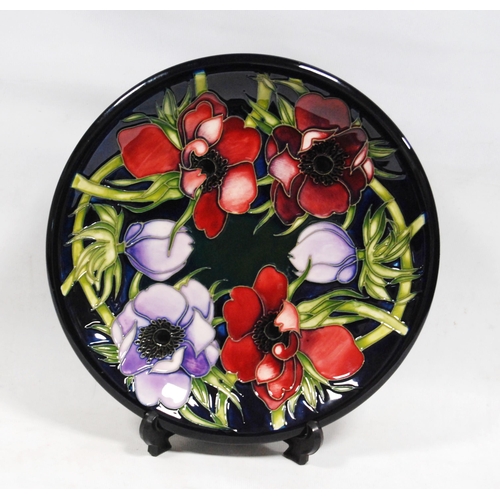 262 - Modern Moorcroft plate decorated with tube lined red and violet anemones with green stalks on a blue... 