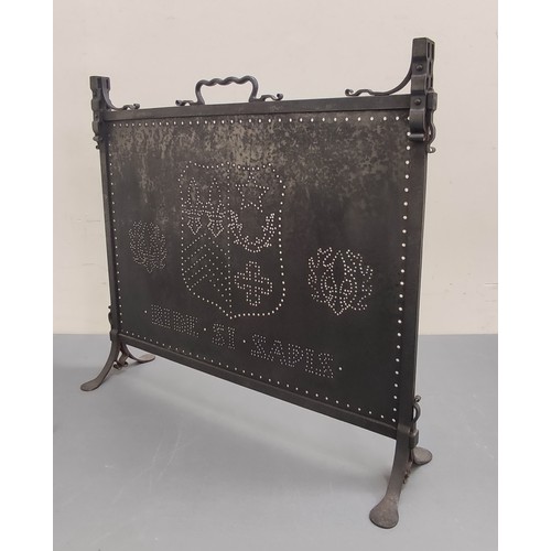 625 - Dark metal firescreen with carrying handle and pierced panel with a coat of arms, on cheval supports... 