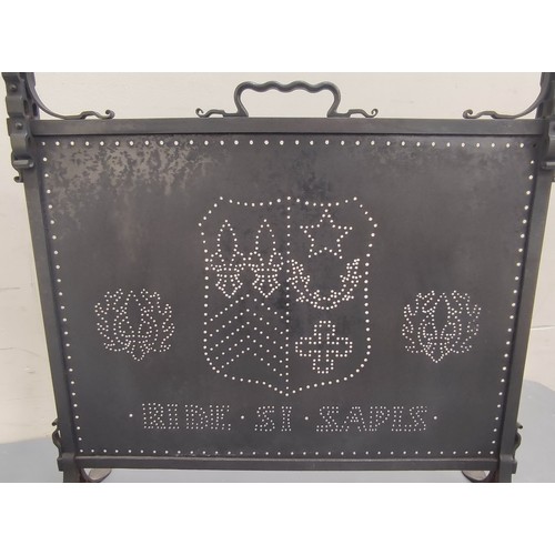 625 - Dark metal firescreen with carrying handle and pierced panel with a coat of arms, on cheval supports... 