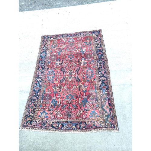 500 - Persian Heriz carpet with stylised flowers and foliage in a red field surrounded by an indigo border... 