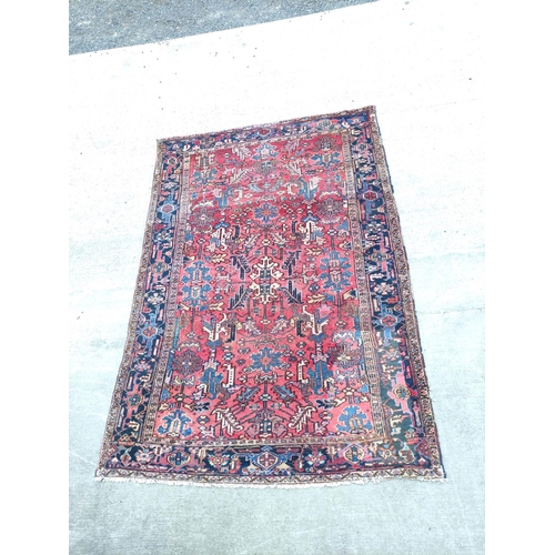 500 - Persian Heriz carpet with stylised flowers and foliage in a red field surrounded by an indigo border... 