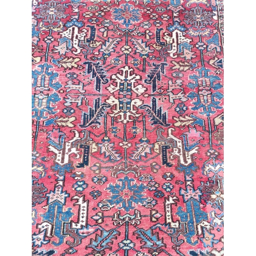 500 - Persian Heriz carpet with stylised flowers and foliage in a red field surrounded by an indigo border... 