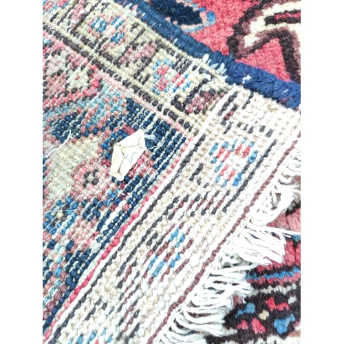 500 - Persian Heriz carpet with stylised flowers and foliage in a red field surrounded by an indigo border... 