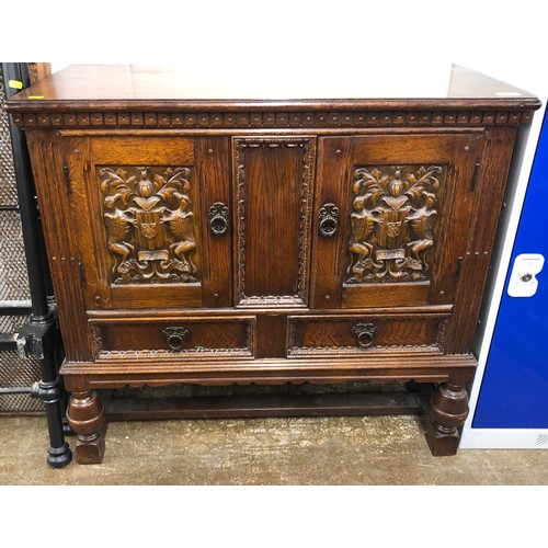 567 - Oak carved cupboard, two doors with carved coats-of-arms, above two drawers, 92 x 43 x 86cm.