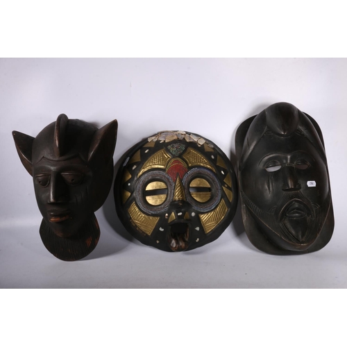 118 - Three African wall face masks, one painted with gilt decoration, 30cm diameter.