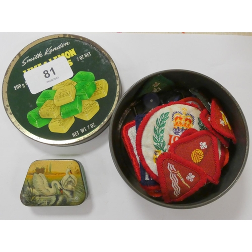 81 - Small hand printed tin 'Swan's on a Lake' scene and tin of Scout badges.