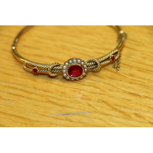 131 - Victorian yellow metal bangle set with seed pearls and faceted red stones, 10g gross. #368