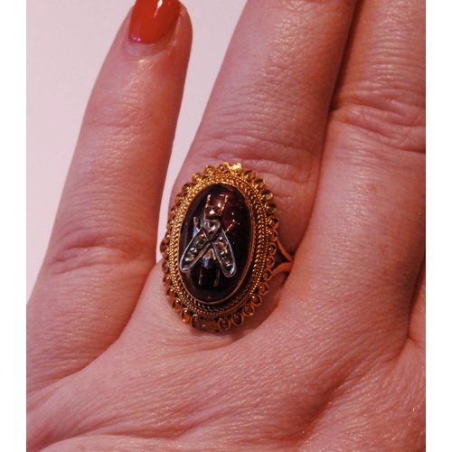 33 - Gold ring with oval cabochon garnet applied with a diamond-set fly, in beaded and twisted mount, the... 