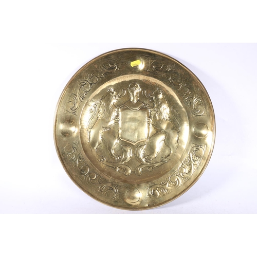 99 - Embossed brass wall charger decorated with central crest, marked J. Co brass, 38cm diameter.