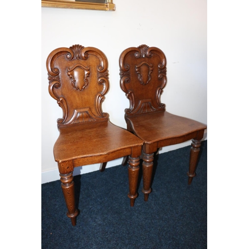 495 - Pair of Victorian carved oak hall chairs, the shield backs with scroll border, raised on turned supp... 