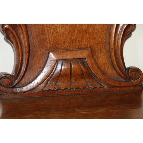 495 - Pair of Victorian carved oak hall chairs, the shield backs with scroll border, raised on turned supp... 