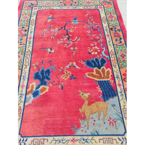 228 - Chinese red ground rug, a deer in the corner below a blossom tree with birds, decorative cream guard... 