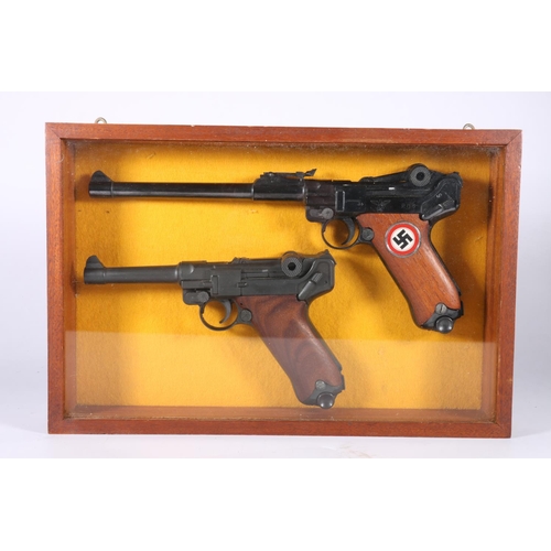 837 - Wall display containing two replica Luger pistols, frame size 24.5cm x 37cm.