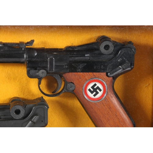 837 - Wall display containing two replica Luger pistols, frame size 24.5cm x 37cm.